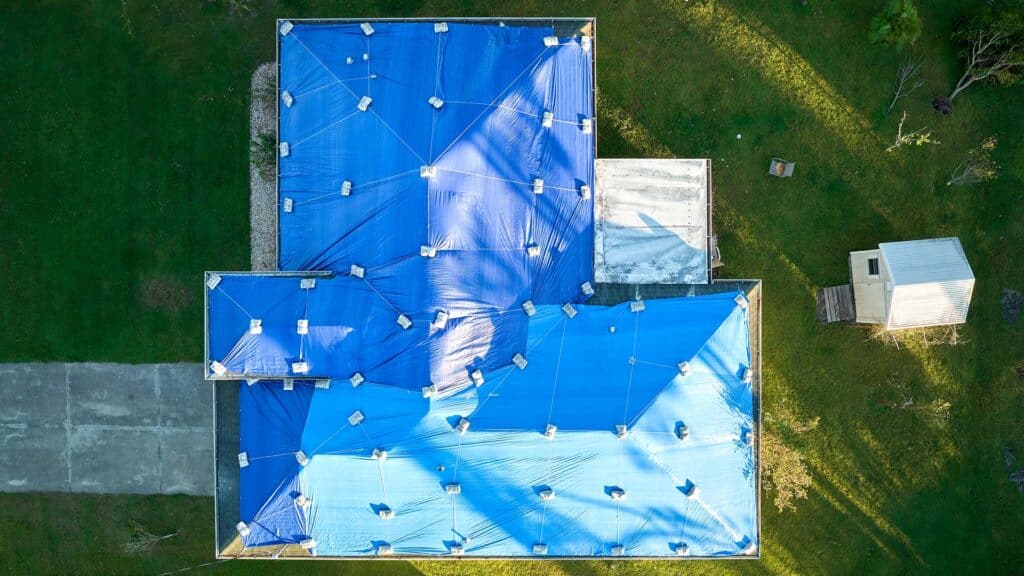 Hurricane Ian damaged house rooftop covered with protective plastic tarp, water damage on the roof, needs roof repair