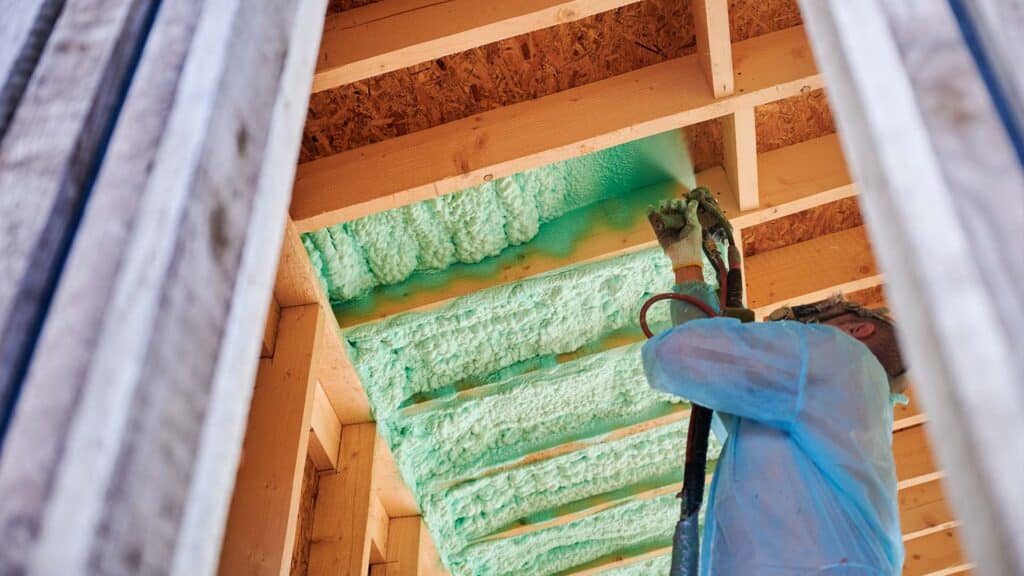 Worker spraying polyurethane foam for insulating wooden frame house, roof insulation is done for roofing energy efficiency